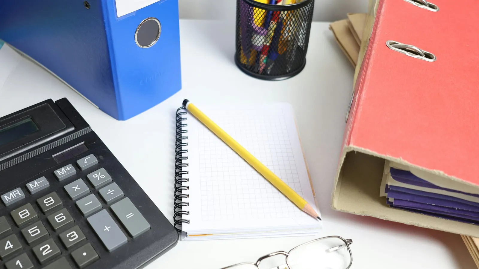 Binders, calculator, notebook, and office supplies on a desk